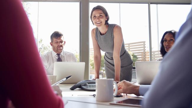 businesswoman stands listening to colleagues at a QGK35YC 1920x1080